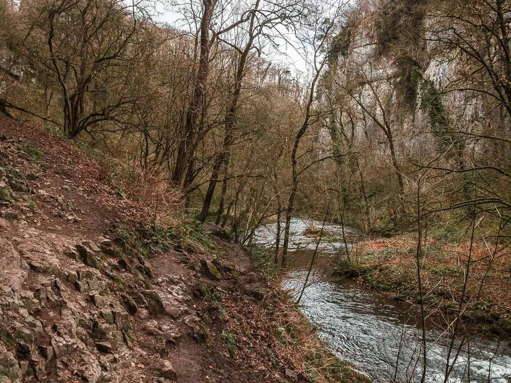 A steep muddy dirt hill on the left, with a trail running across it, with the river below to the right.