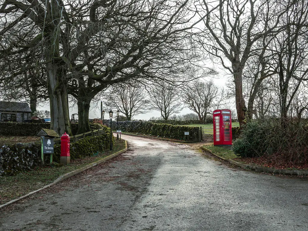 A road, with a red post box on the left, and red telephone box on the right.