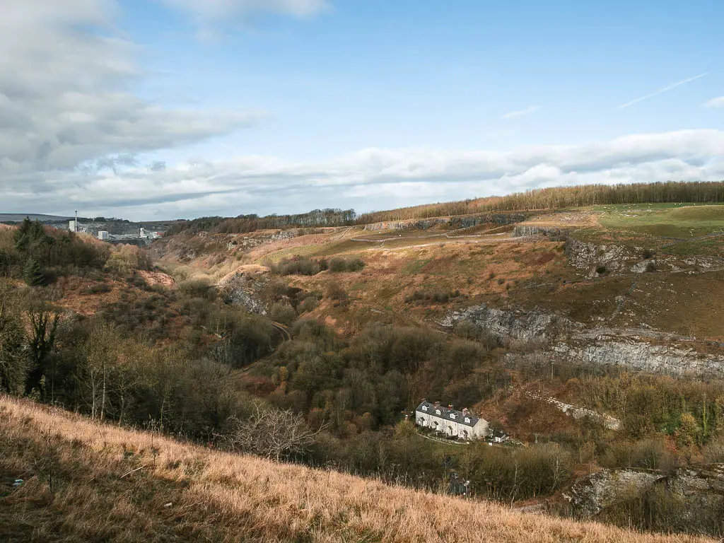 Looking down into the valley full of green and brown woodland trees, and a white coloured cottage nestled on the middle, at the start of the walk down to Chee Dale and the stepping stones.