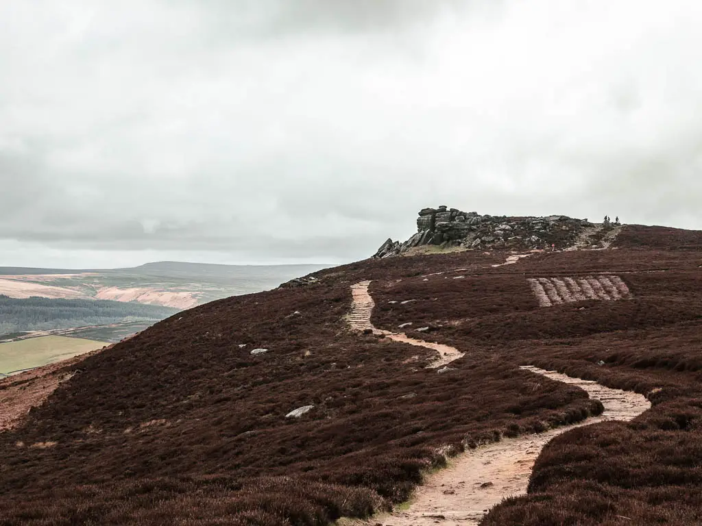 A trail snaking along the top of Derwent Edge, leading to a tor ahead. There is a view down to the valley to the left.