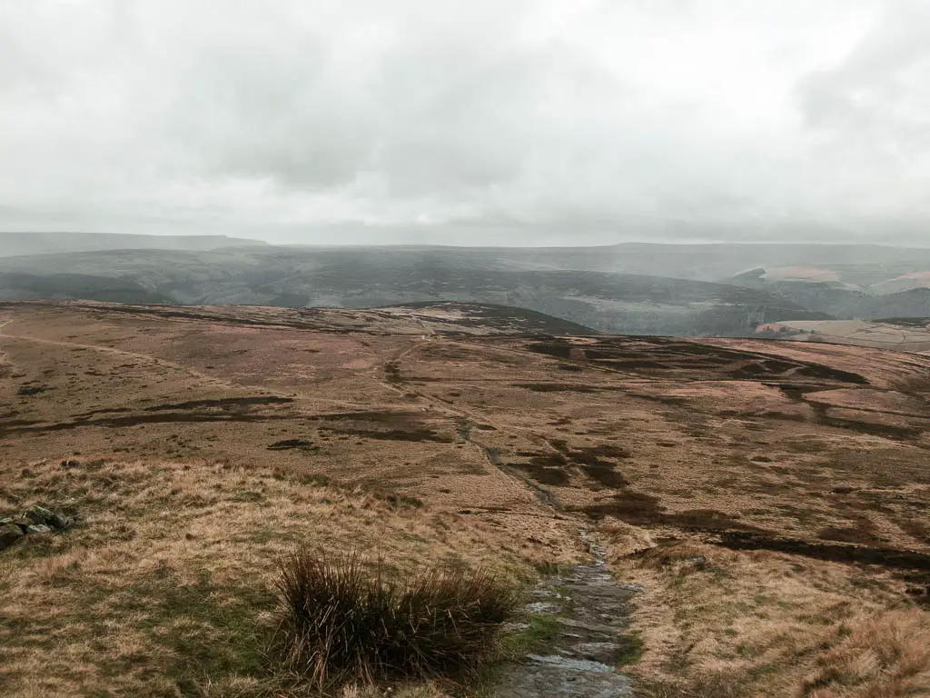A dirt trail leading downhill on the walk off Derwent Edge. It leads towards the vast moorland, on a misty overcast day.