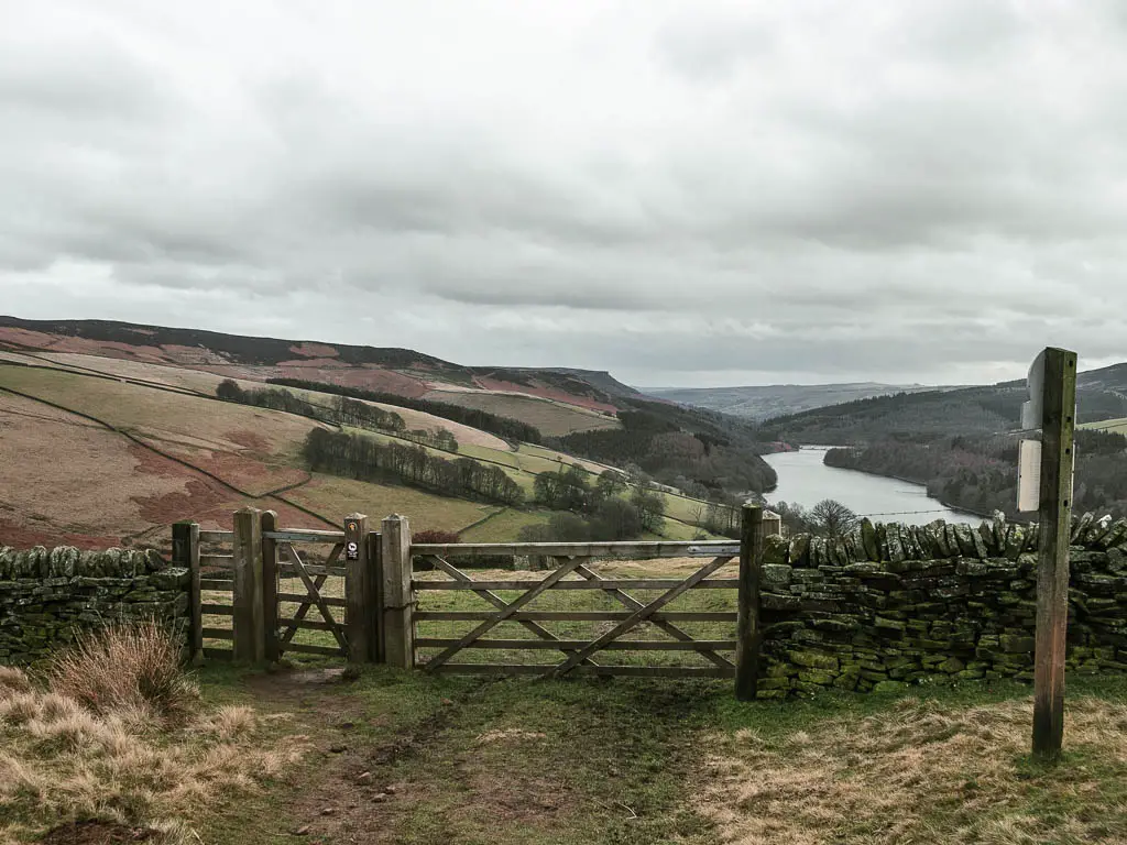 A wooden gate, leading to a field, with the reservoir down below.