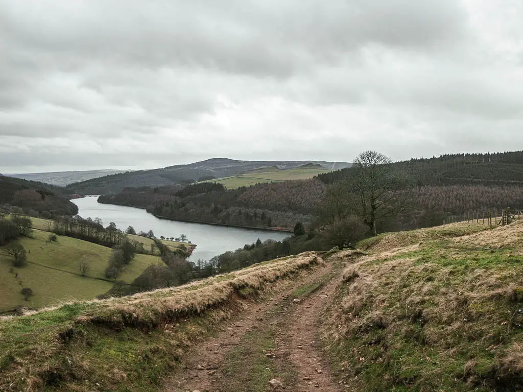 A dirt track trail leading downhill through the grass towards the reservoir below. 
