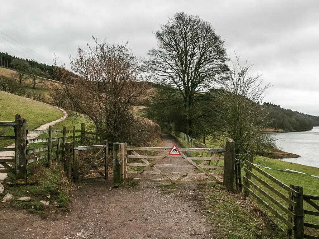 A trail leading through a wooden gate, with the reservoir to the right.