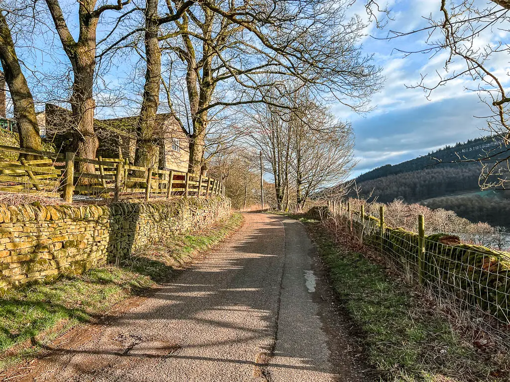 A country road lined with a metal fence and stone wall, with a house to the left side.