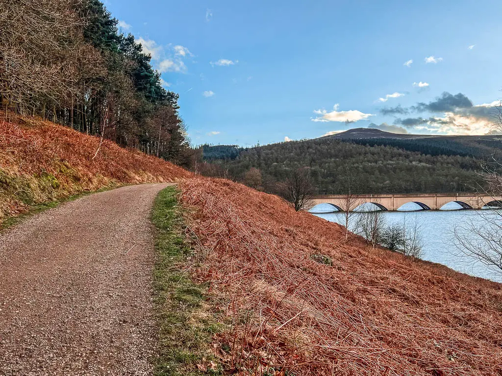 A wide gravel trail on the left, with the reservoir to the right and the arches of the Ashropton viaduct ahead.