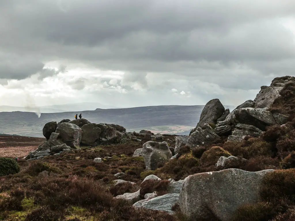 Looking through the rocks at the top of the walk to Simon's Seat. There are people walking on top of some of the rocks ahead. It's a grey cloudy day.