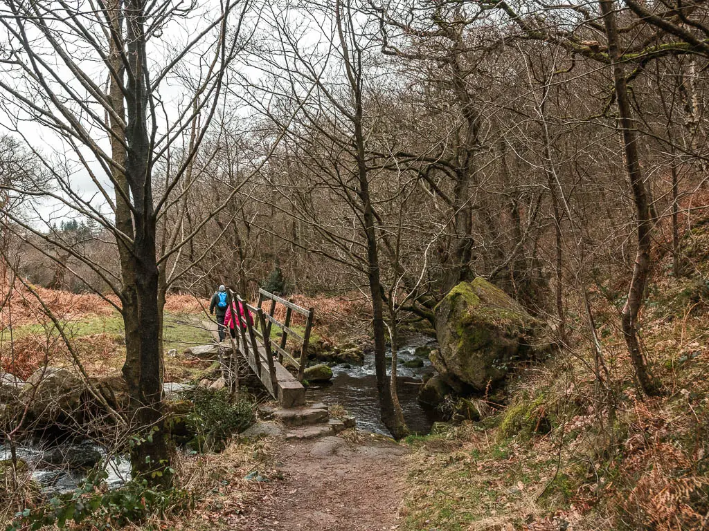 Two people walking across a wooden bridge over the river, in the Valley of Desolation, on the walk towards the waterfall.