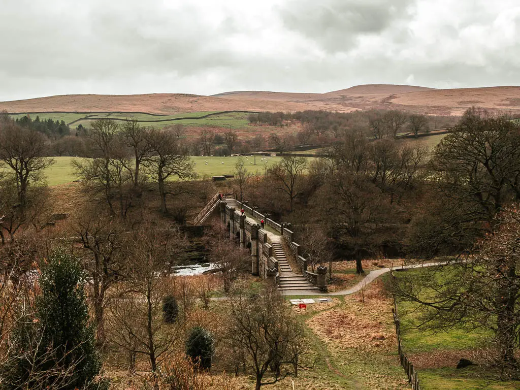 Looking down towards the large bridge across the river, with a few people walking over it, and a view to the hills in the distance.
