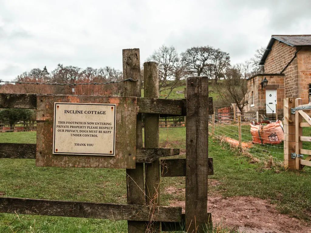 A wooden fence with a sign for the cottage, which is just visible to the right.