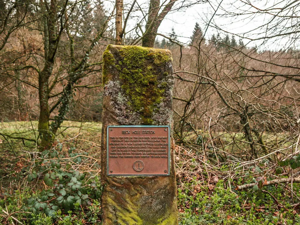 A stone stump with a metal plaque, marking the location of the old Beck Hole Station, along the rail trail walk from Goathland to Grosmont.