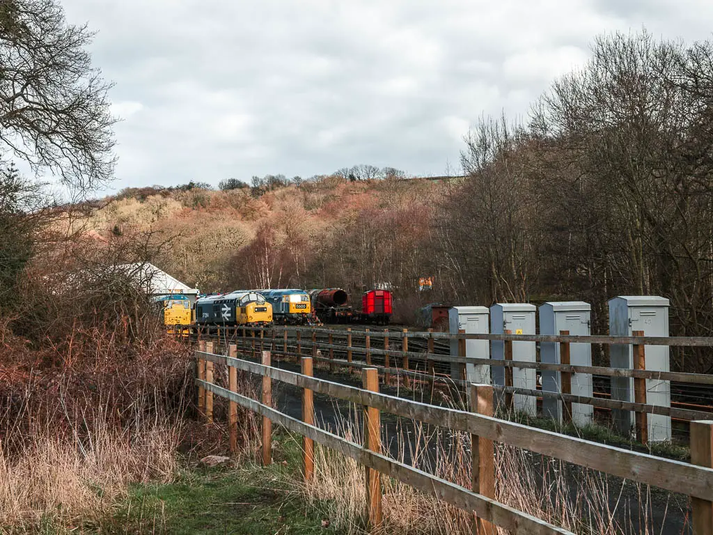 Looking over wooden railings towards a few trains sitting on the end of the railway line.