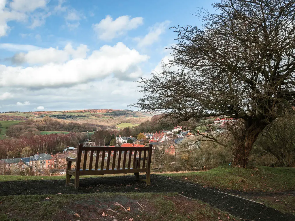 A wooden viewpoint bench, with a view down into the valley and the rooftops of the village of Grosmont.