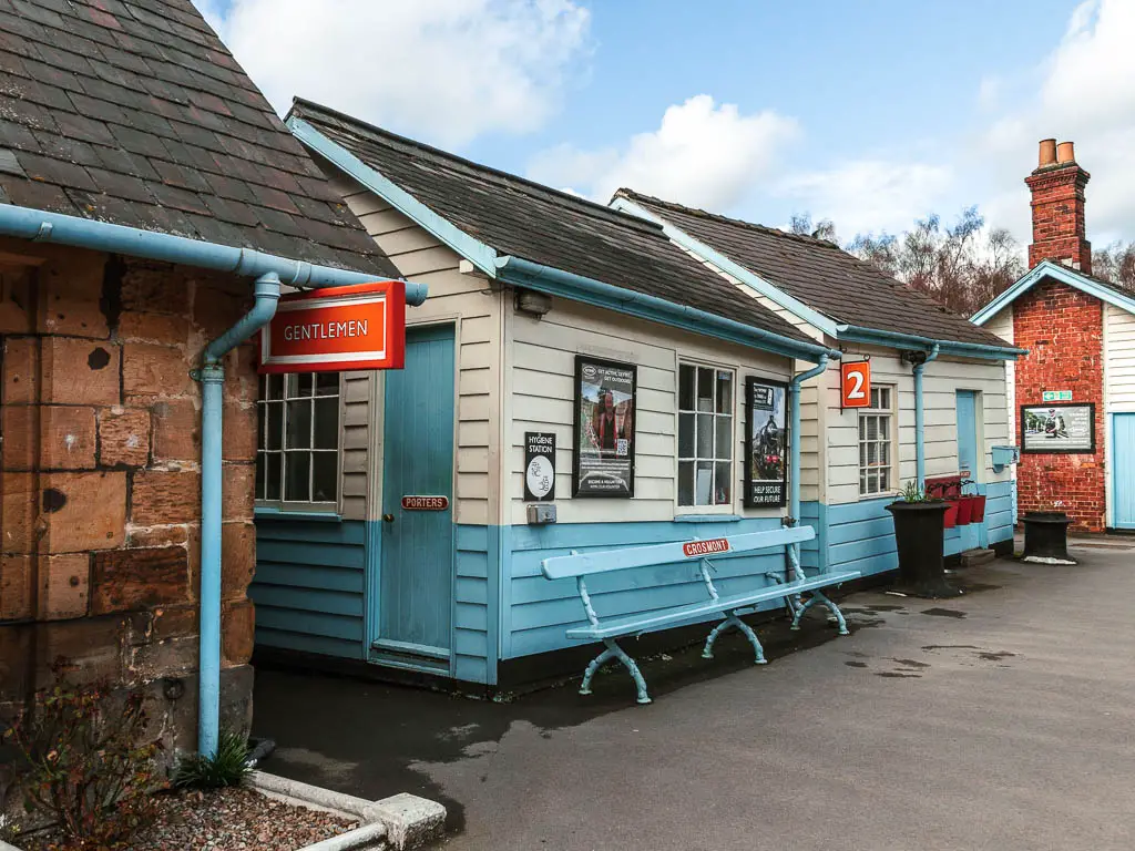 White and blue hut buildings in Grosmont train station. There is an orange hanging sign saying 'gentlemen', and another sign with the platform number 2 written on it.