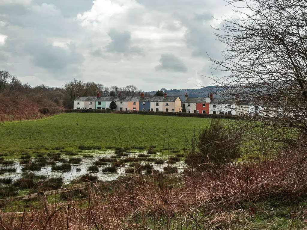 Looking across the body grass field to a row of colourful houses in the Esk Valley, partway along the walk from Goathland to Grosmont.