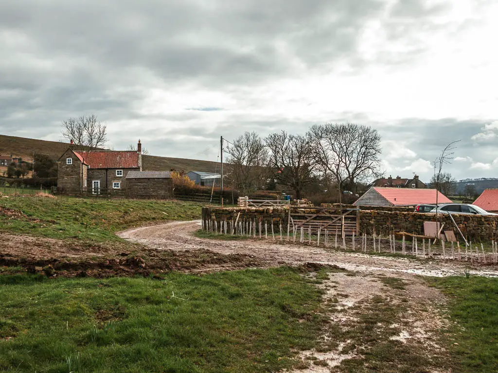 Farm buildings with red roofs, and a dirt road curving through the middle.