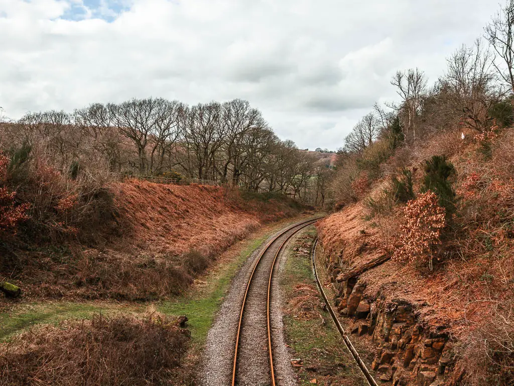 Looking down and along the railway line as it curves right, along the Goathland to Grosmont circular walk. The rail track is at the bottom of two banks with bushes and trees.