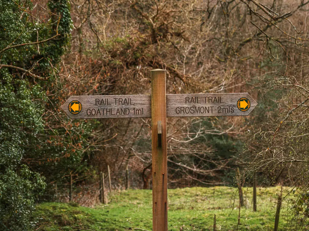 A wooden trail signpost pointing left to walk to Goathland along the rail trail, and right to walk to Grosmont.