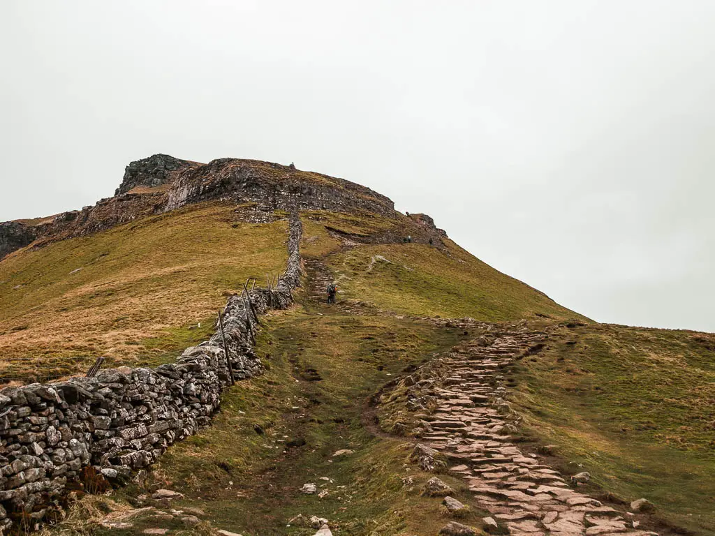 A rugged stone paved trail on the right, and a stone wall on the left, with Pen-y-Ghent straight ahead.