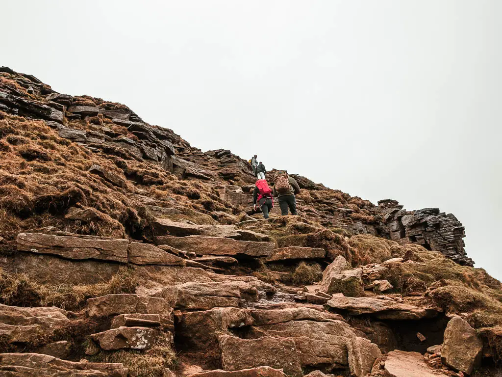 A hillside covered in large rocks, and a few people walking up them ahead.