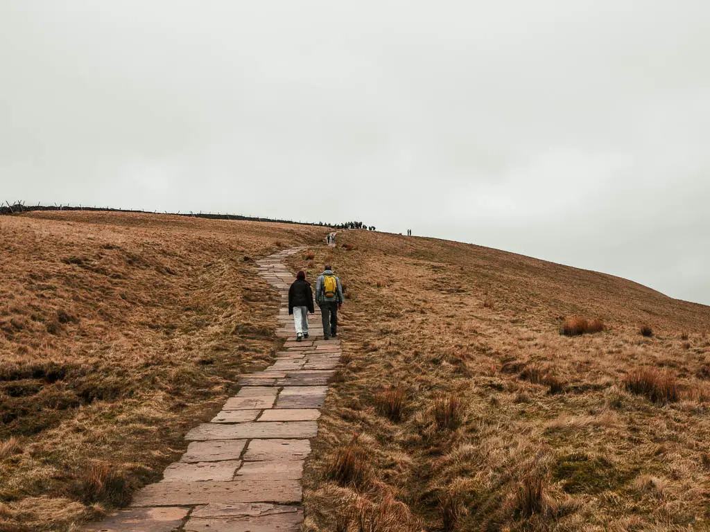 A neat stone paved trail leading up towards the summit of Pen-y-Ghent, near the end of the walk to the top. There are a couple of people walking ahead on the trail, and a mass of people visible ahead on the summit.