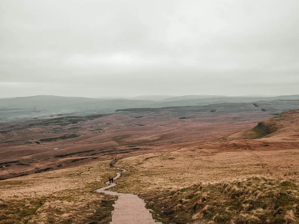 A trail snaking downhill with a view ahead to the vast landscape which looks like the moon. 