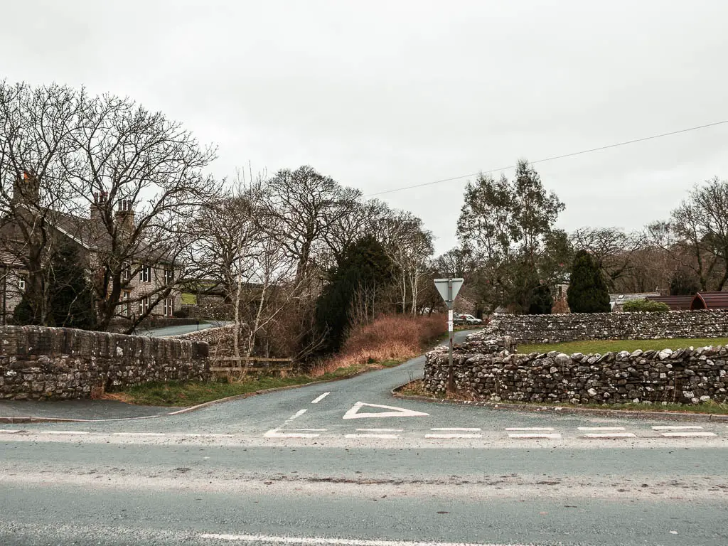 Looking across the road to a side road lined with a few trees and stone walls.