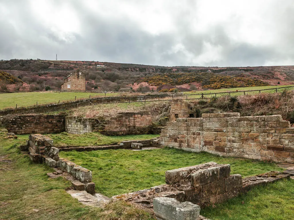 The stone walled ruins in a grass field.