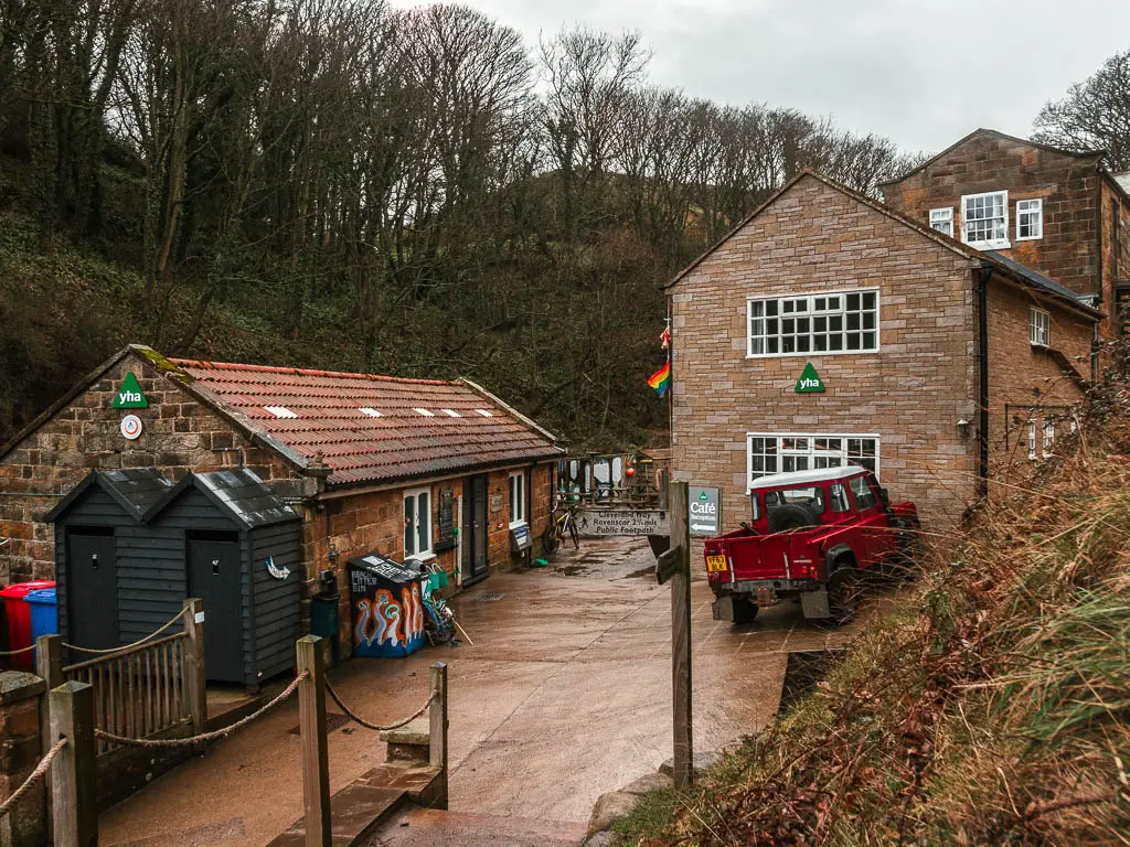 Looking down towards the buildings of the Boggle Hole Youth Hostel. There is a red pick up truck parked outside.