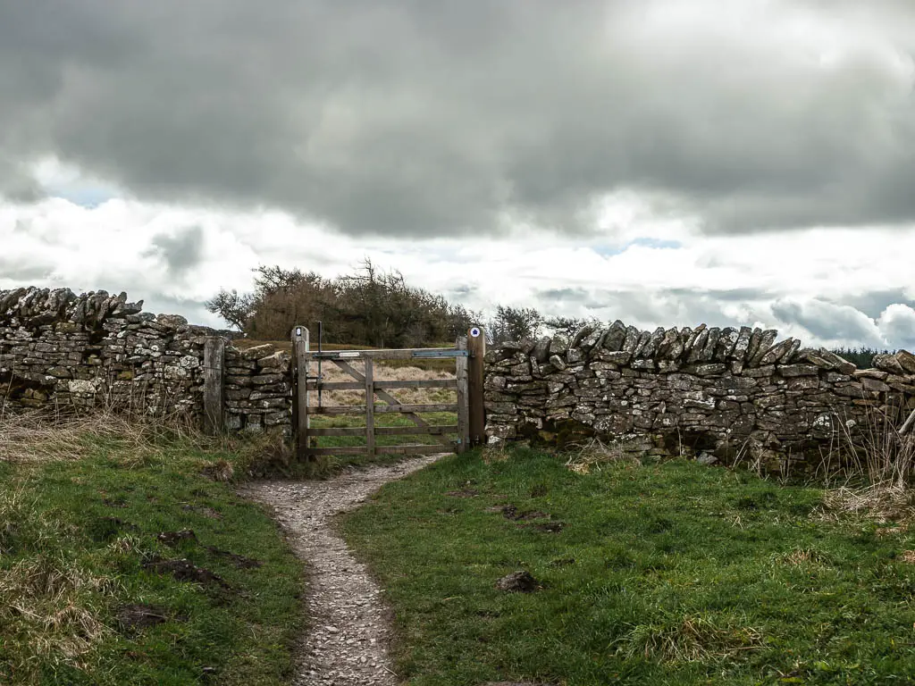 A trail leading to a wooden gate in a stone wall.