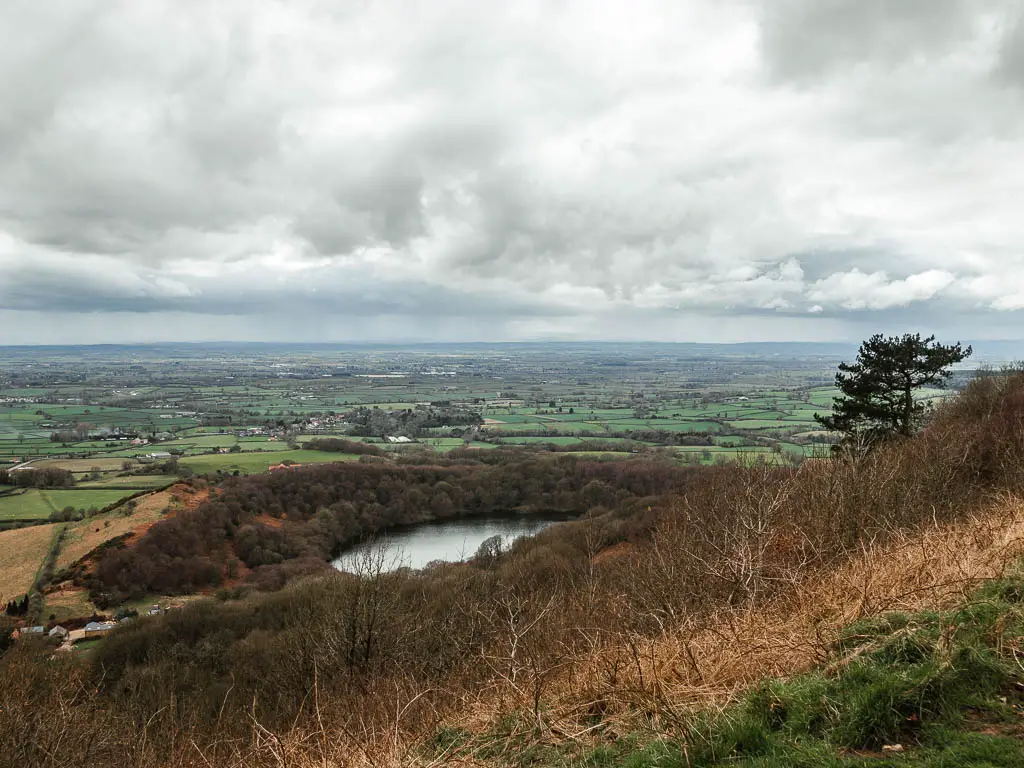 Looking down tho the circle shaped Gormire lake surround by woodland trees, when walking along the top of Sutton Bank.