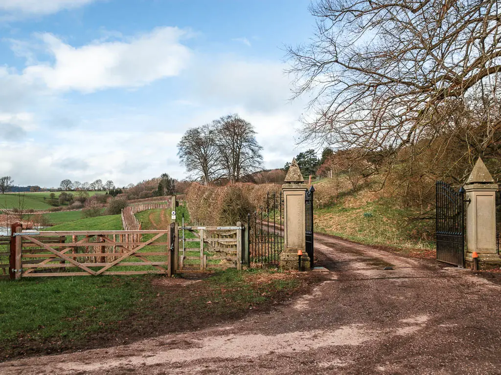 A grand gate entrance to the right, and wooden gate to the left leading onto a grass trail.