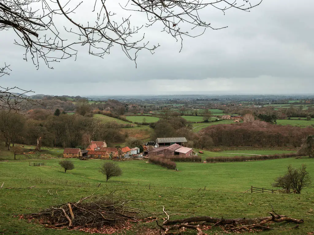 Looking down the large grass field to a group of farm buildings below, and field views as far as the eye can see beyond.