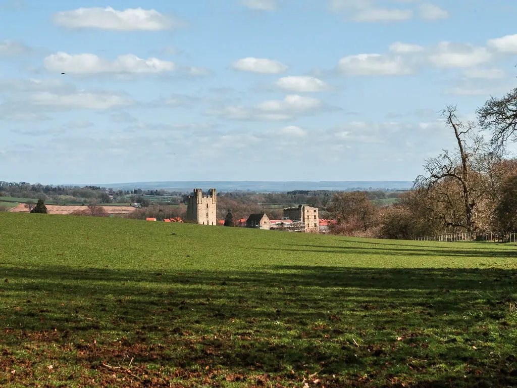 Looking across the grass field to the top of the ruins of the castle in Helmsley in the distance. 