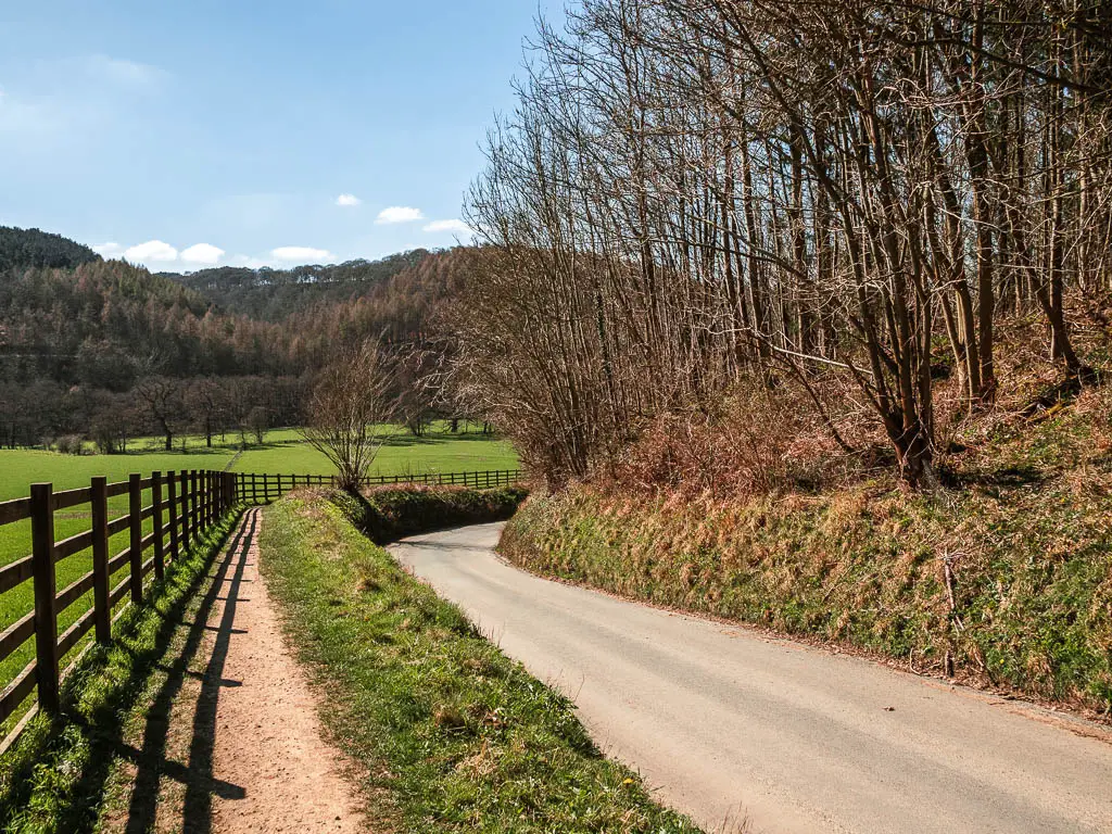 A road leading ahead and to the right,  lined with a grass backs on wither side, with a small path on the left side. 