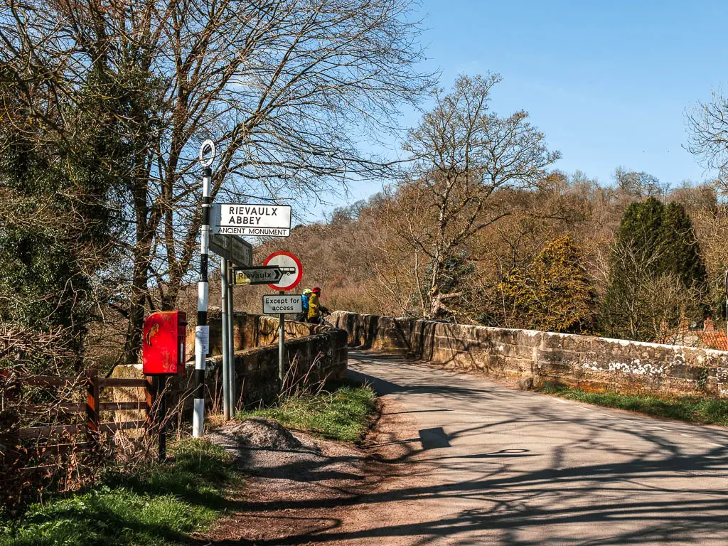 A bridge with a white and black stripped signpost next to it pointing right to walk to Rievaulx Abbey.