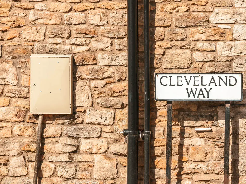 A white street sign on a stone wall saying 'Cleveland Way'.