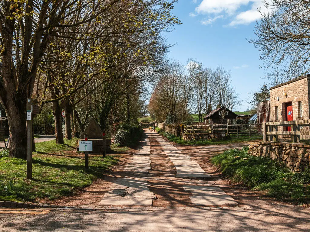 A road leading straight, with woodland to the left and a stone shed building to the right/