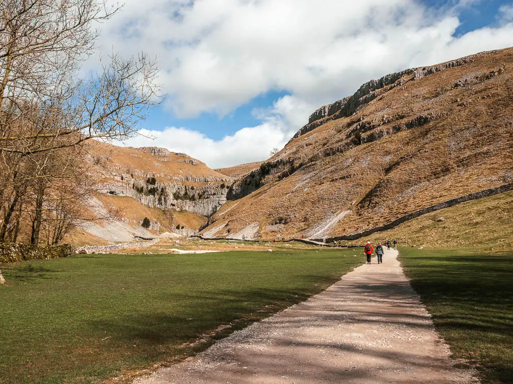 A wide path leading through a large grass field with the big gorge ahead, on the walk into Gordale Scar. There are lots of people walking on the path.
