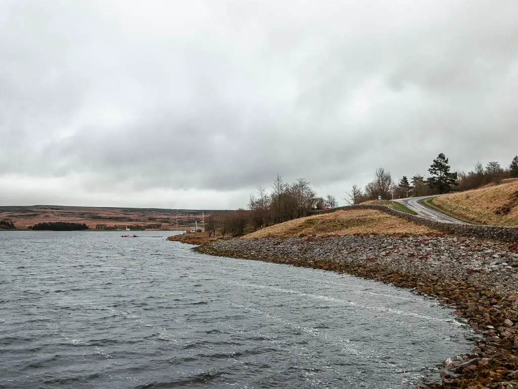 The water lined with a stone bank, and the road leading uphill to the right of it.