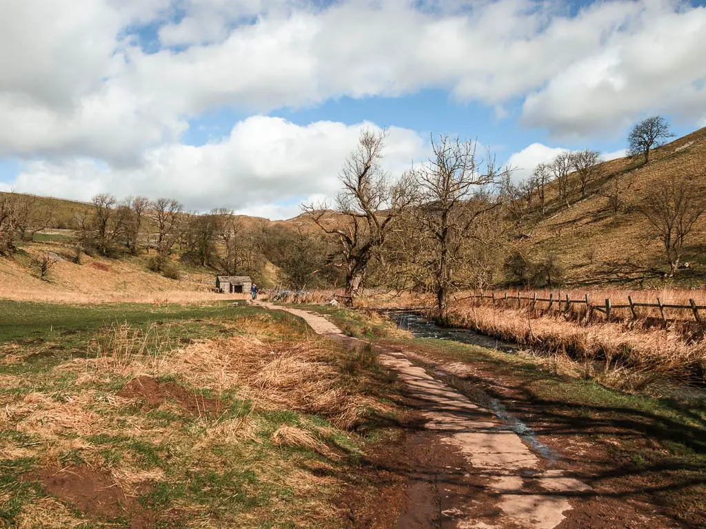 A paved trail leading towards a hut and the hills, on the walk towards Janet's Foss.