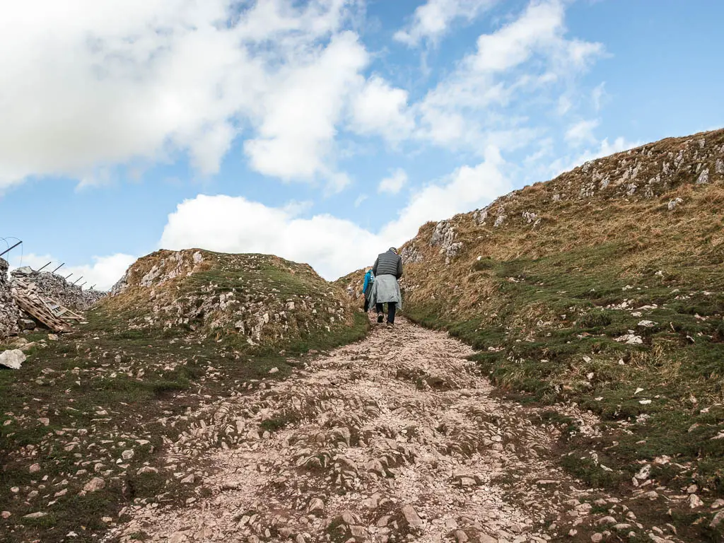 A rocky uphill trail, with a few people walking up it.