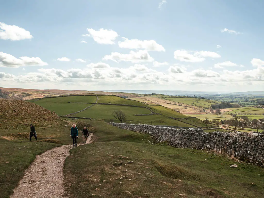 Looking down the trail to the hills in the distance on the walk up to Malham Cove. There are a few people walking up the trail.