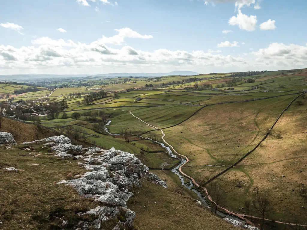 Looking down to the fields below with a stream of water snaking along it, on the walk along the top of Malham Cove.
