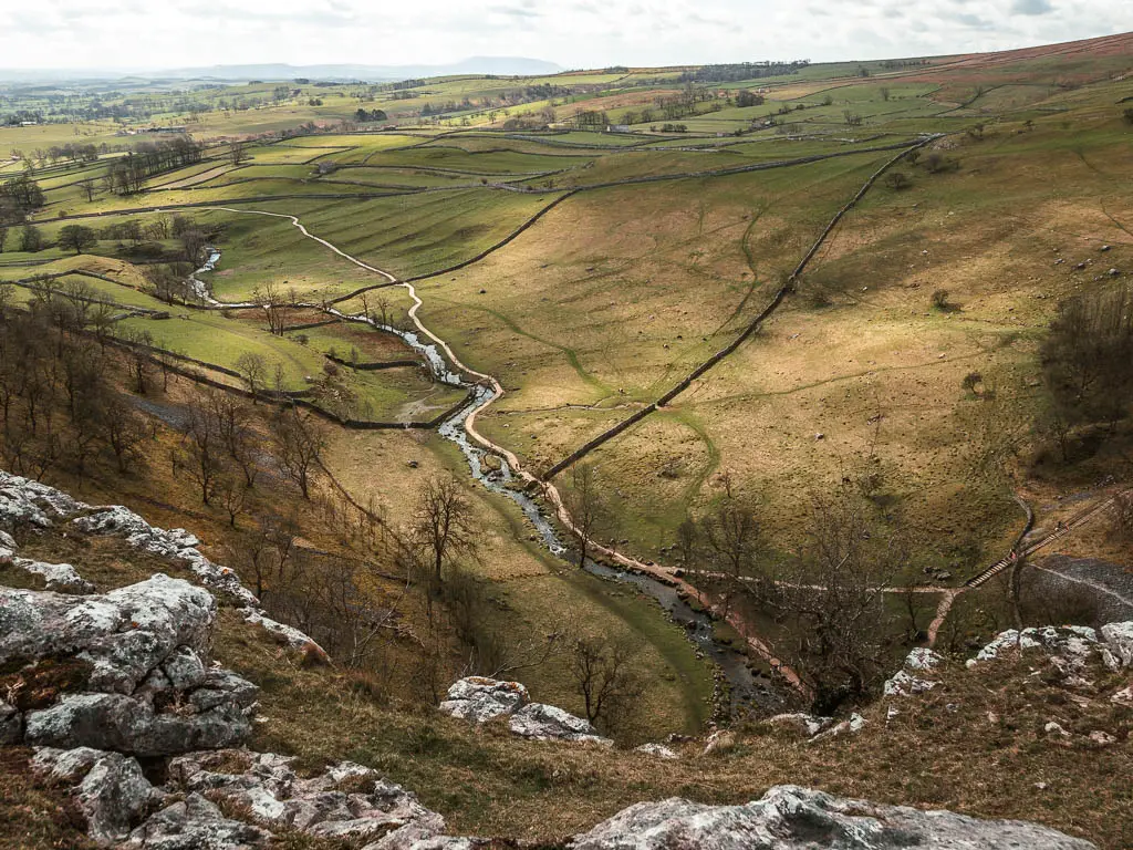 Looking down to the fields below with a stream of water snaking along it, on the walk along the top of Malham Cove.