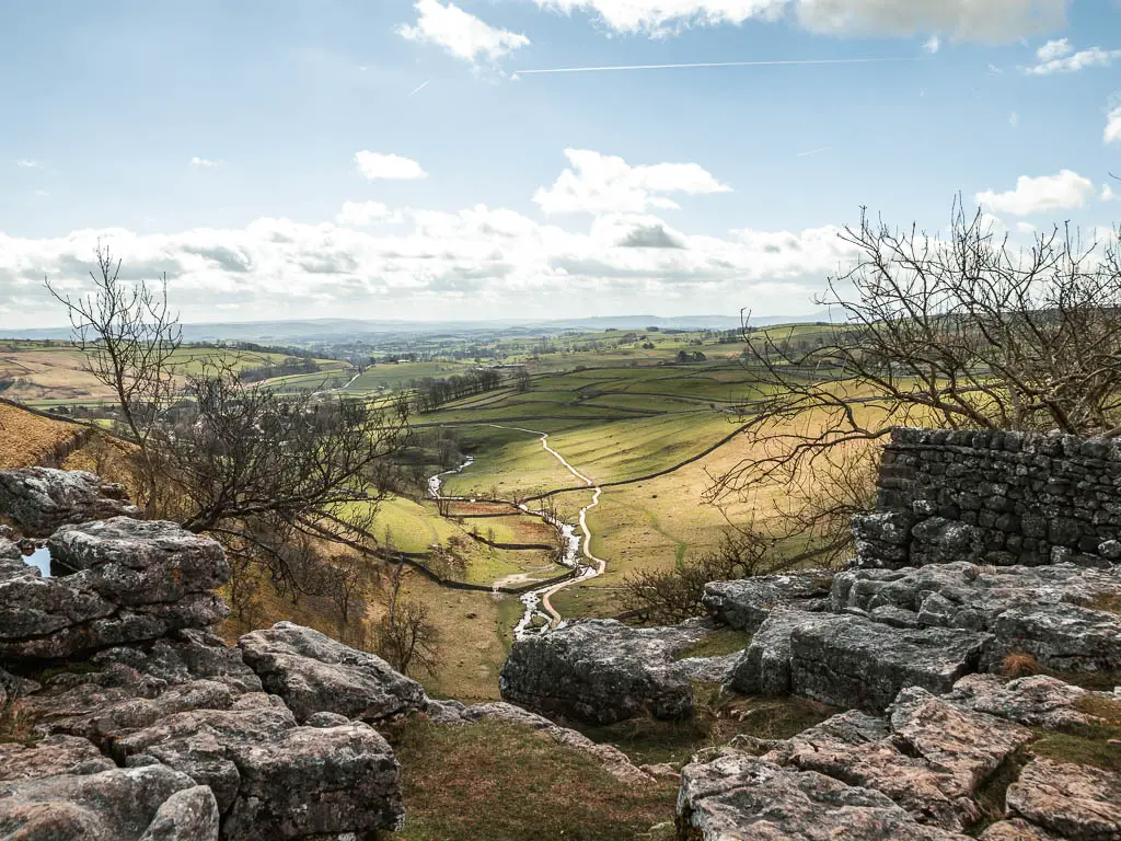 Looking over the rocks, and down into the valley with a river snaking through it, on the walk across Malham Cove.