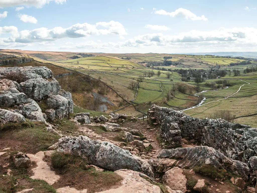 Looking down across the rocks, with a stone wall with a gap on the right, and the valley below, on the walk down from Malham Cove.