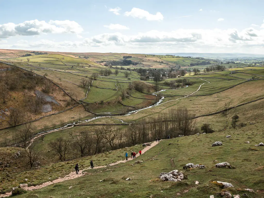 Looking down at the path and river running through the valley on the walk down from Malham Cove. There are lots of people walking along the path.