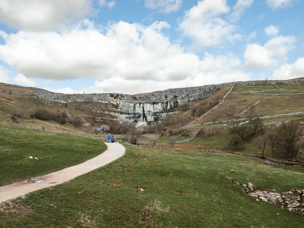 A path leading towards the cliff face of Malham Cove, with a few people walking along it.