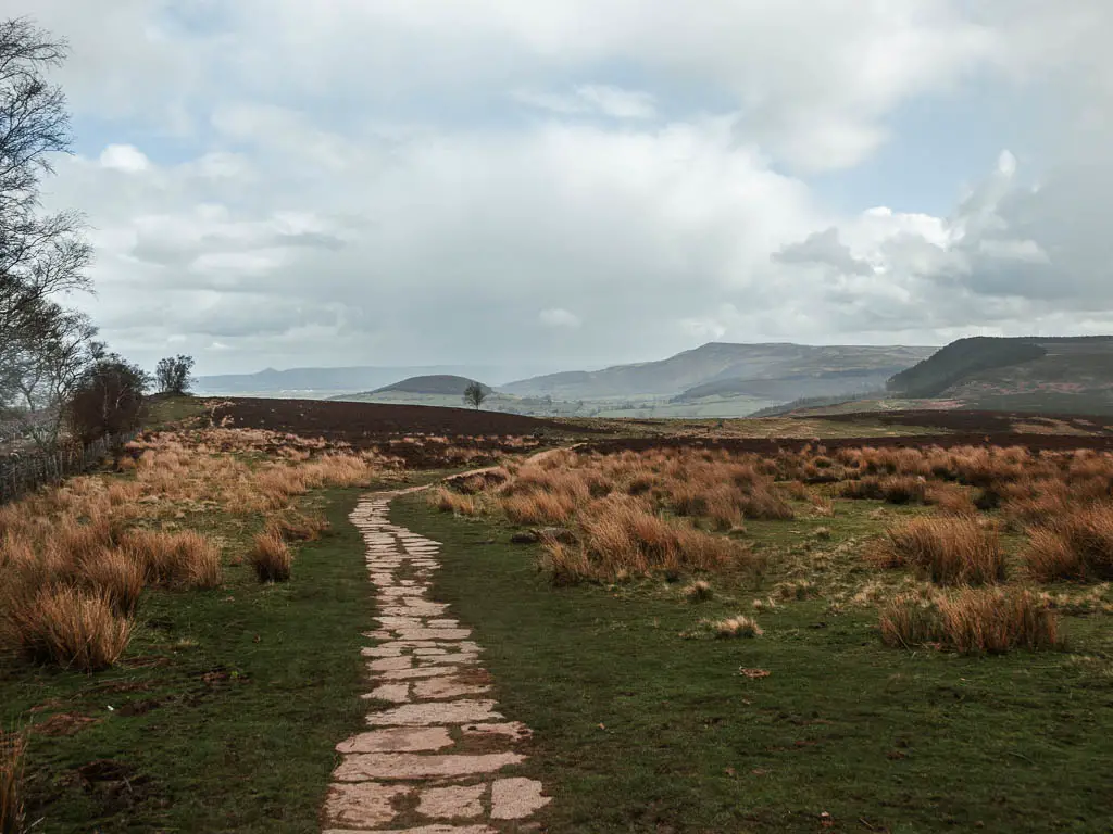 A paved trail running through the Scarth Wood Moor, with a view to the hills in the distance, along the circular Osmotherley walk route.